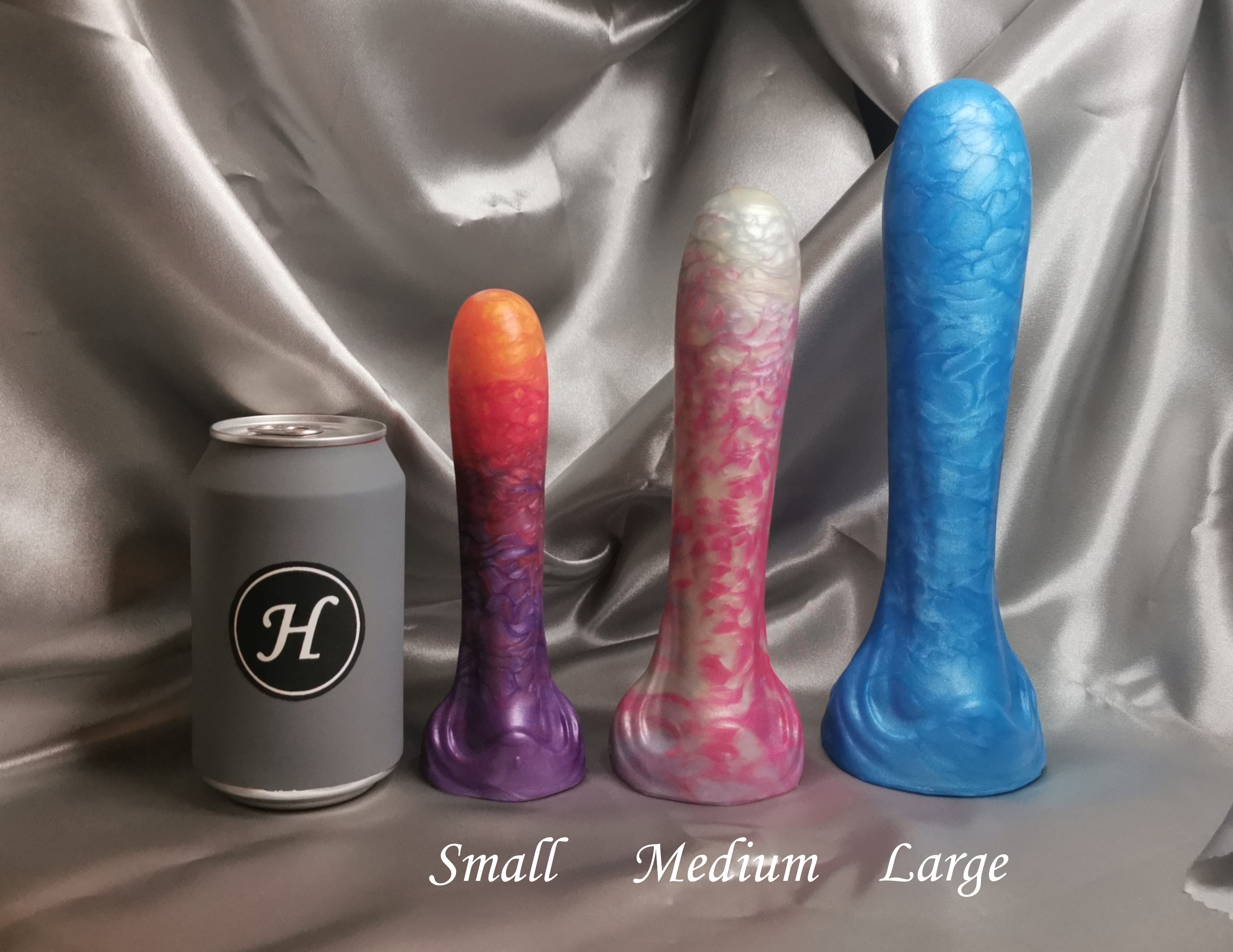 Three colorful dildos labeled 'Small', 'Medium', and 'Large' next to a can with a logo on a silver fabric background.